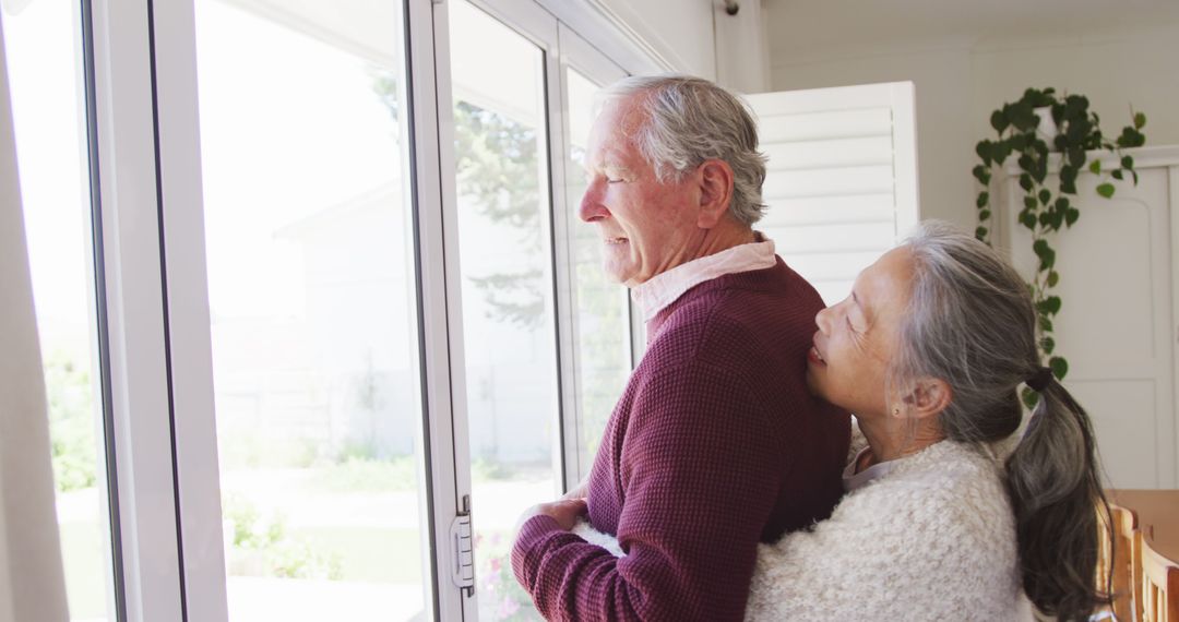Elderly Couple Embracing and Gazing Out Window at Home