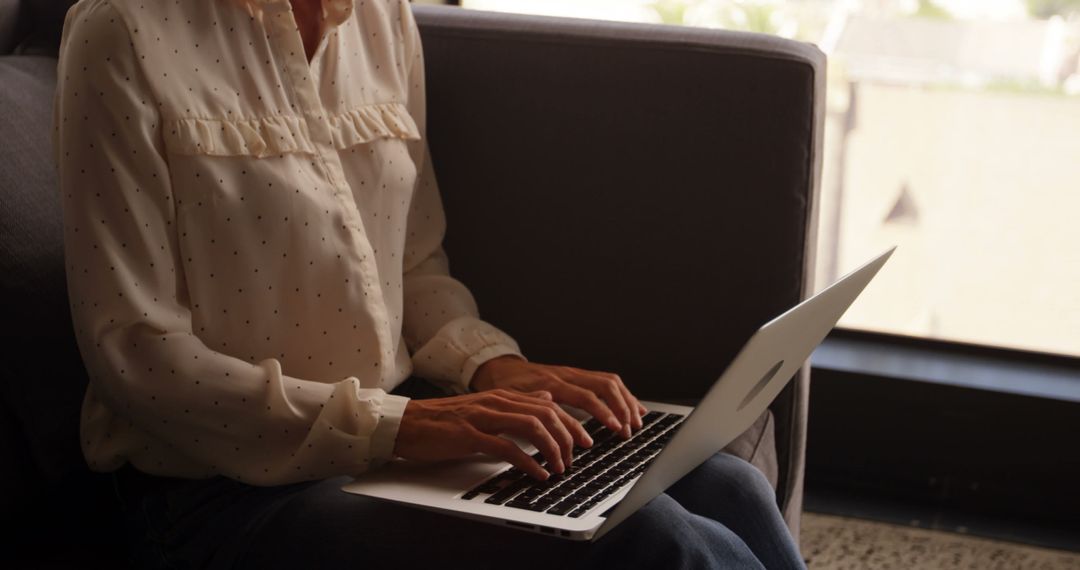 Woman Typing on Laptop Sitting on Couch by Window - Free Images, Stock Photos and Pictures on Pikwizard.com