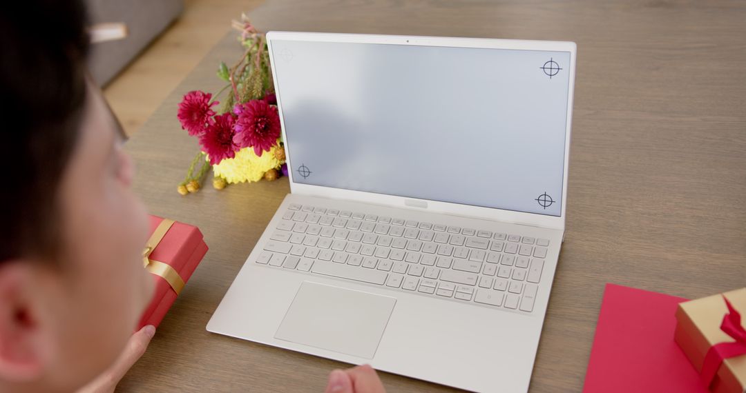 Man Video Calling on White Laptop with Gifts On Table