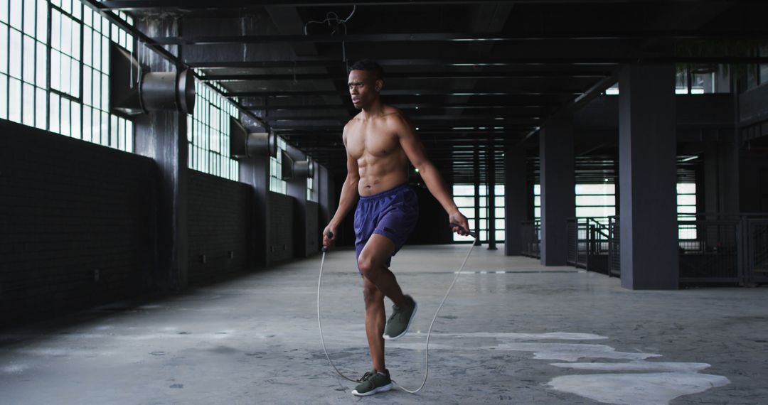 Shirtless african american man skipping the rope in an empty urban building - Free Images, Stock Photos and Pictures on Pikwizard.com