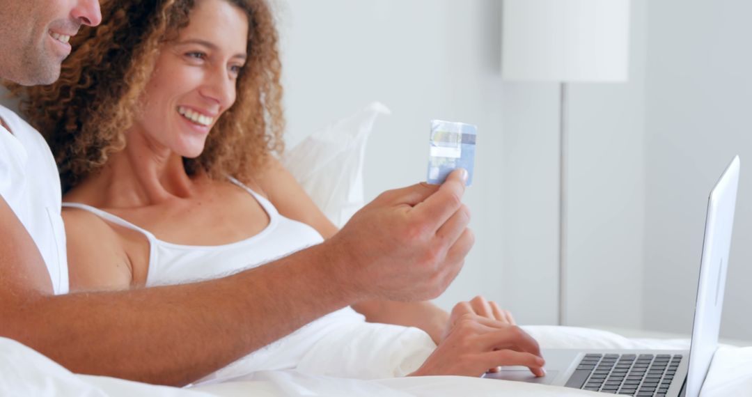 Smiling Couple Online Shopping in Bed with Credit Card