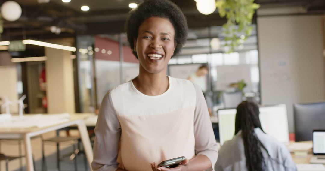 Smiling African American Woman Holding Smartphone in Modern Office - Free Images, Stock Photos and Pictures on Pikwizard.com