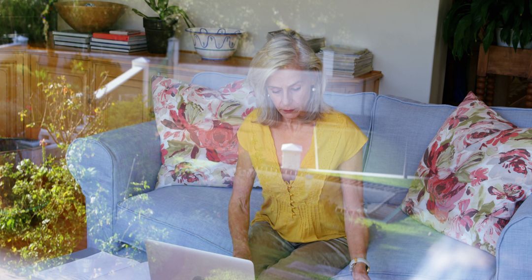 Senior Woman Working on Laptop at Home Surrounded by Nature Reflection - Free Images, Stock Photos and Pictures on Pikwizard.com