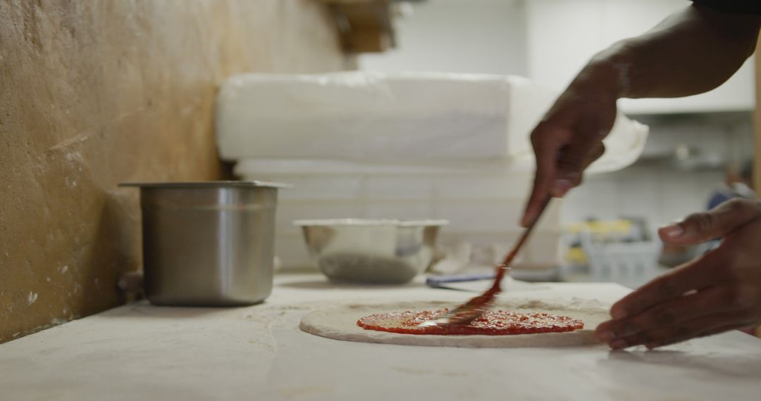 Chef spreading tomato sauce on pizza dough in restaurant kitchen - Free Images, Stock Photos and Pictures on Pikwizard.com