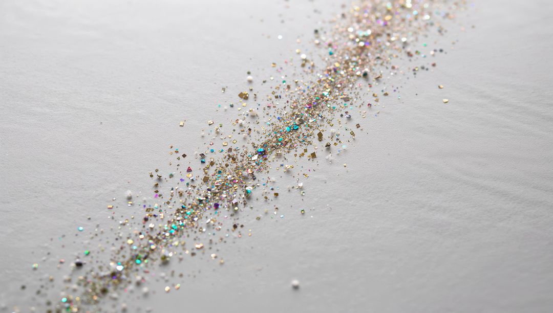 Glittering diagonal trail of iridescent gold and silver sequins on white textured paper