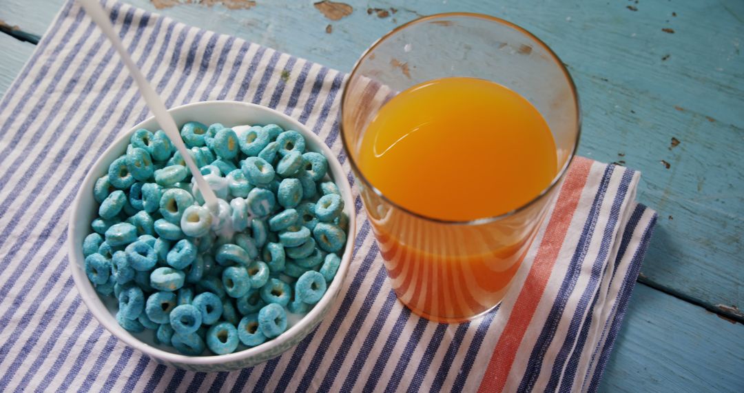 Bowl of Blue Cereal with Orange Juice on Striped Kitchen Towel - Free Images, Stock Photos and Pictures on Pikwizard.com