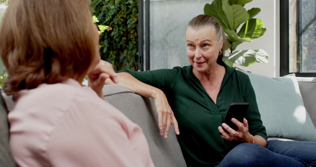 Mature Friends Engaging Conversation on Comfortable Sofa with Smartphone