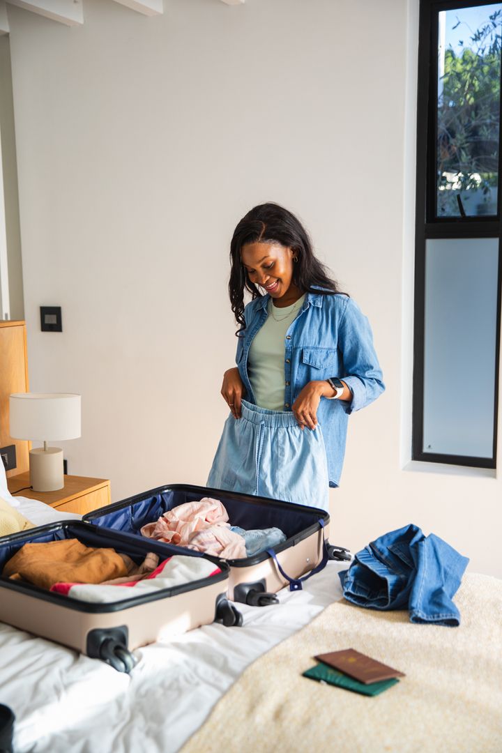 Woman Packing for Travel Standing Next to Open Suitcase on Bed