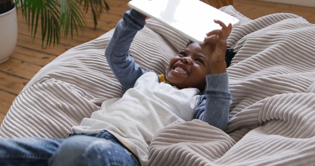 Happy Child Enjoying Tablet on Cozy Chair Indoors - Free Images, Stock Photos and Pictures on Pikwizard.com