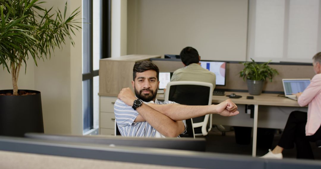 Businessman Stretching while Colleagues Work on Laptops