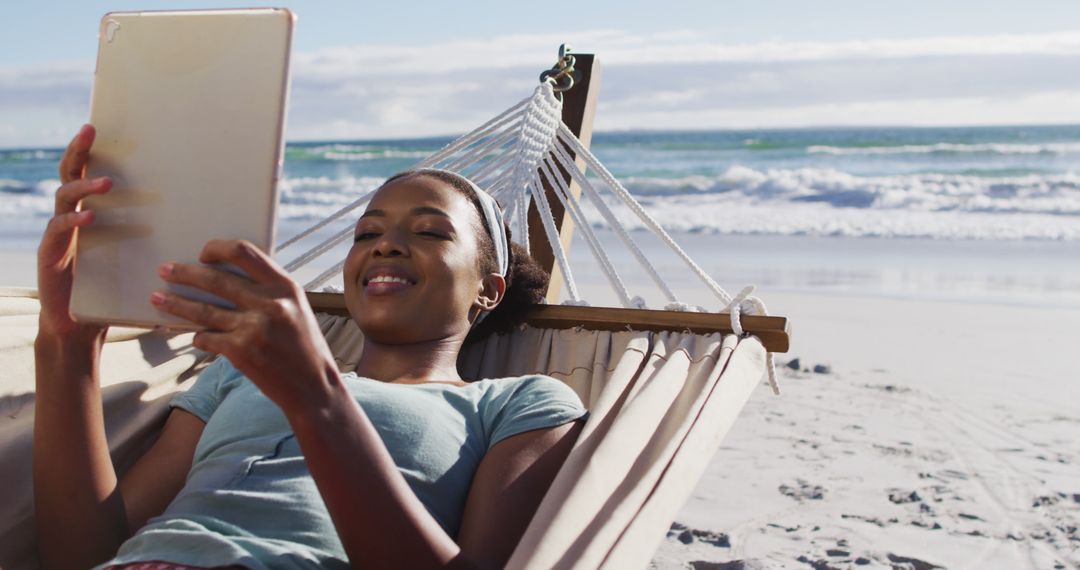African american woman using digital tablet while lying on a hammock at the beach - Free Images, Stock Photos and Pictures on Pikwizard.com