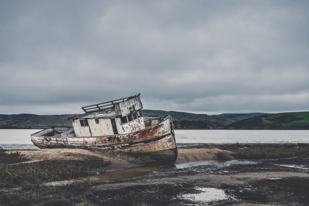 Abandoned Fishing Boat on Muddy Shoreline Under Cloudy Sky - Free Images, Stock Photos and Pictures on Pikwizard.com