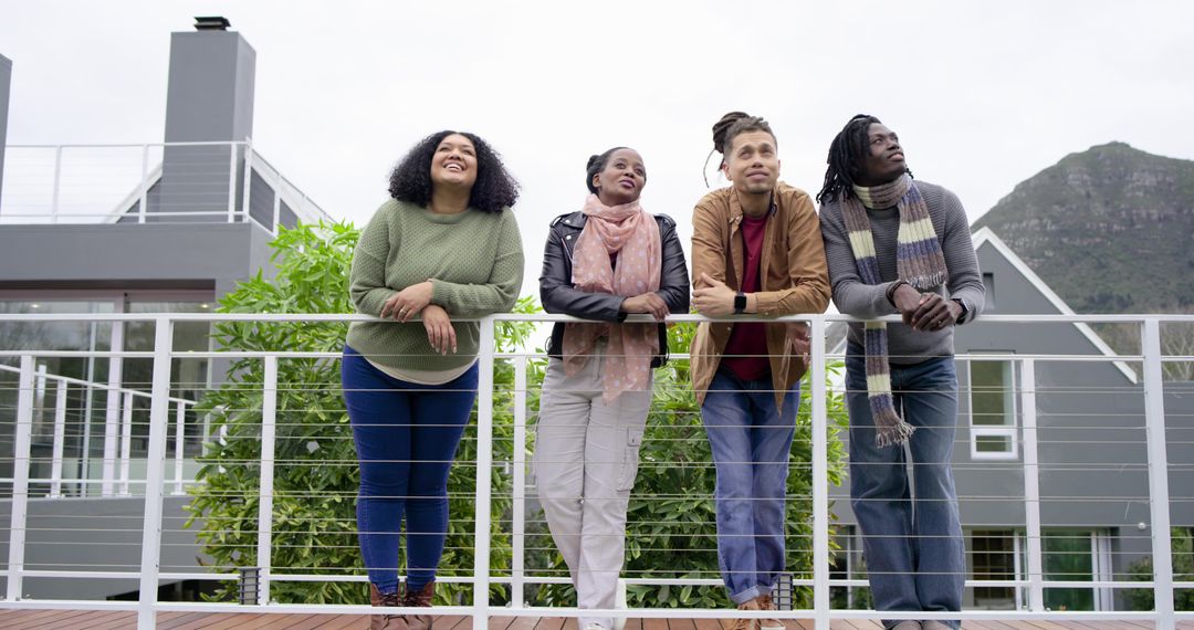 Diverse friends leaning on balcony railing relaxing and gazing at mountain view