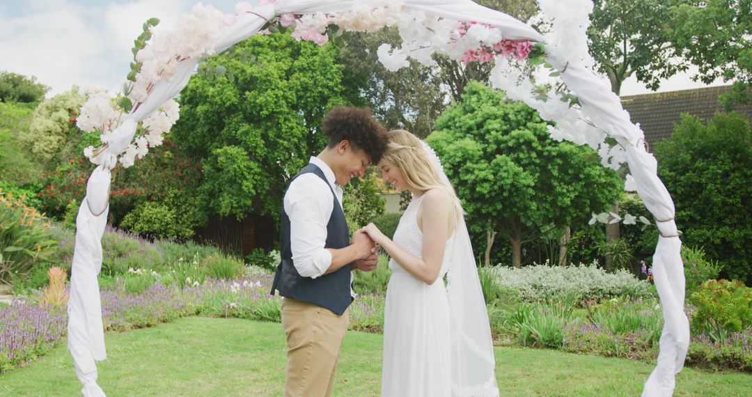 Newlyweds Embracing Under Floral Arch in Sunny Garden