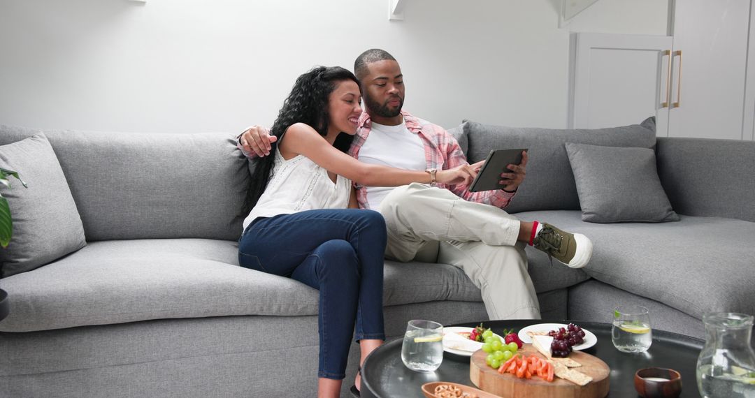 Relaxed Couple Enjoying Tablet Time with Fruit Snacks at Home