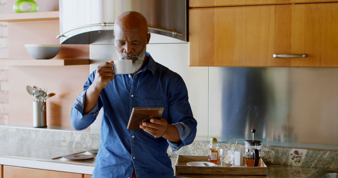 Elderly Man Reading Tablet while Drinking Coffee in Modern Kitchen - Free Images, Stock Photos and Pictures on Pikwizard.com