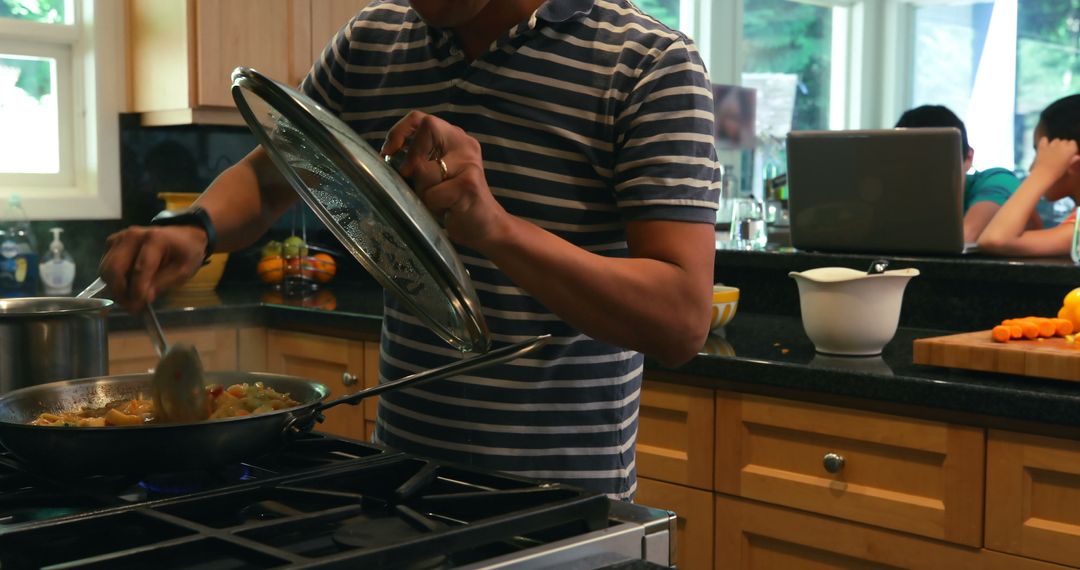 Father Cooking in Kitchen with Children on Laptop in Background - Free Images, Stock Photos and Pictures on Pikwizard.com