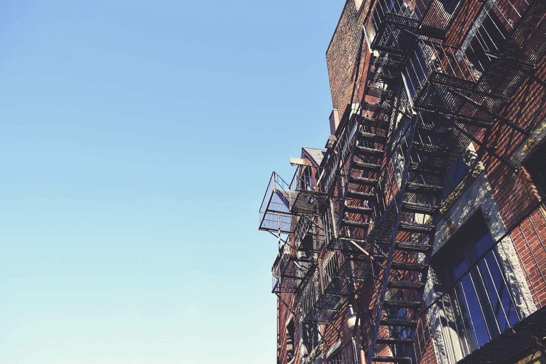 Fire escapes on urban brick building with blue sky backdrop - Free Images, Stock Photos and Pictures on Pikwizard.com