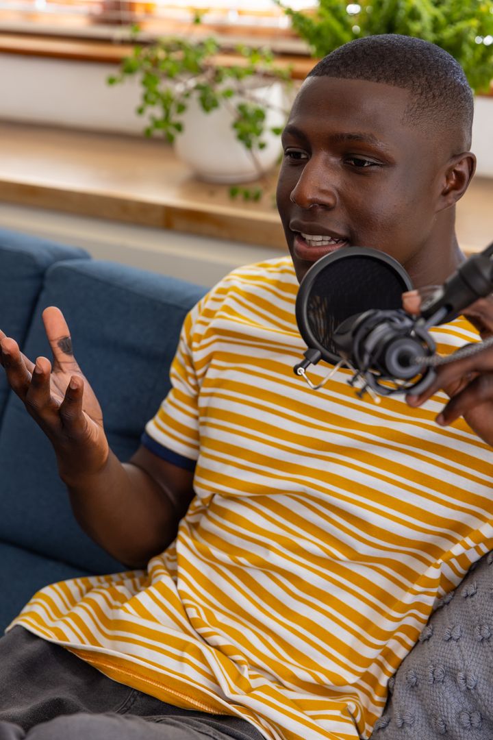 African American man podcasting at home studio on couch with professional microphone
