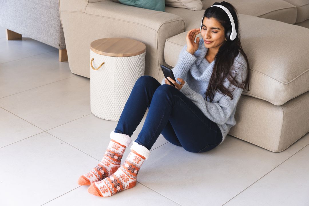 Woman in Cozy Sweater Enjoys Music on Smartphone at Home