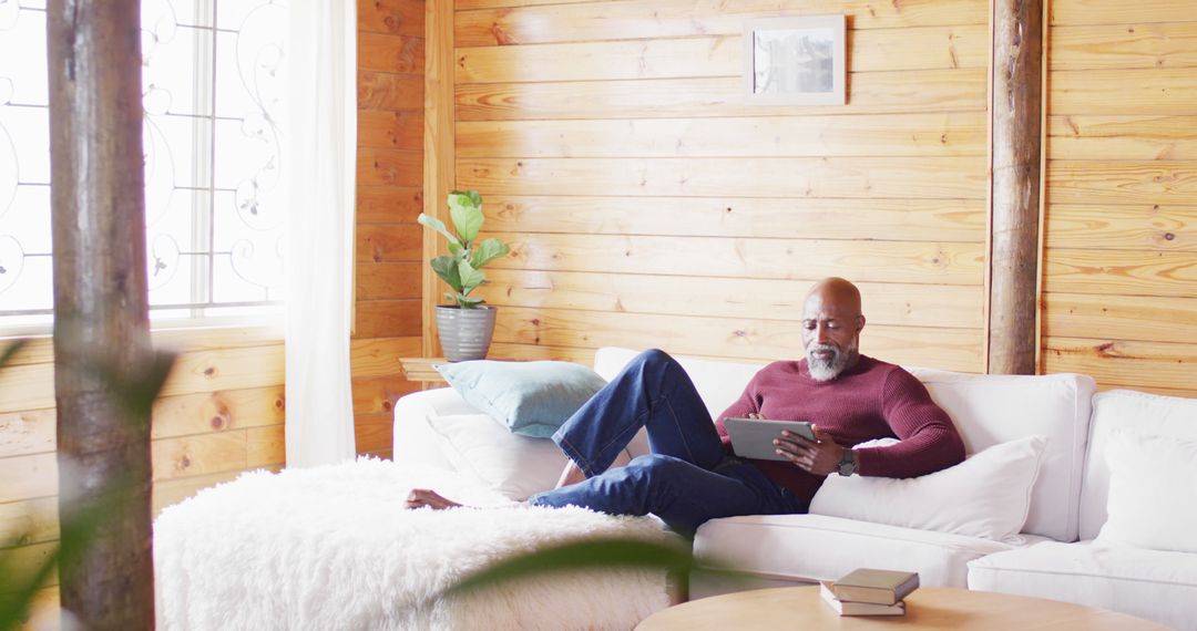 Mature Man Relaxing on Sofa Using Tablet in Cozy Wooden Cabin - Free Images, Stock Photos and Pictures on Pikwizard.com