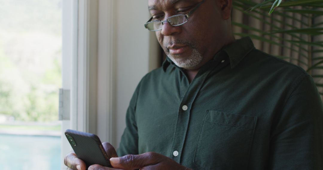 Senior Man Engaging with Smartphone Near Window - Free Images, Stock Photos and Pictures on Pikwizard.com