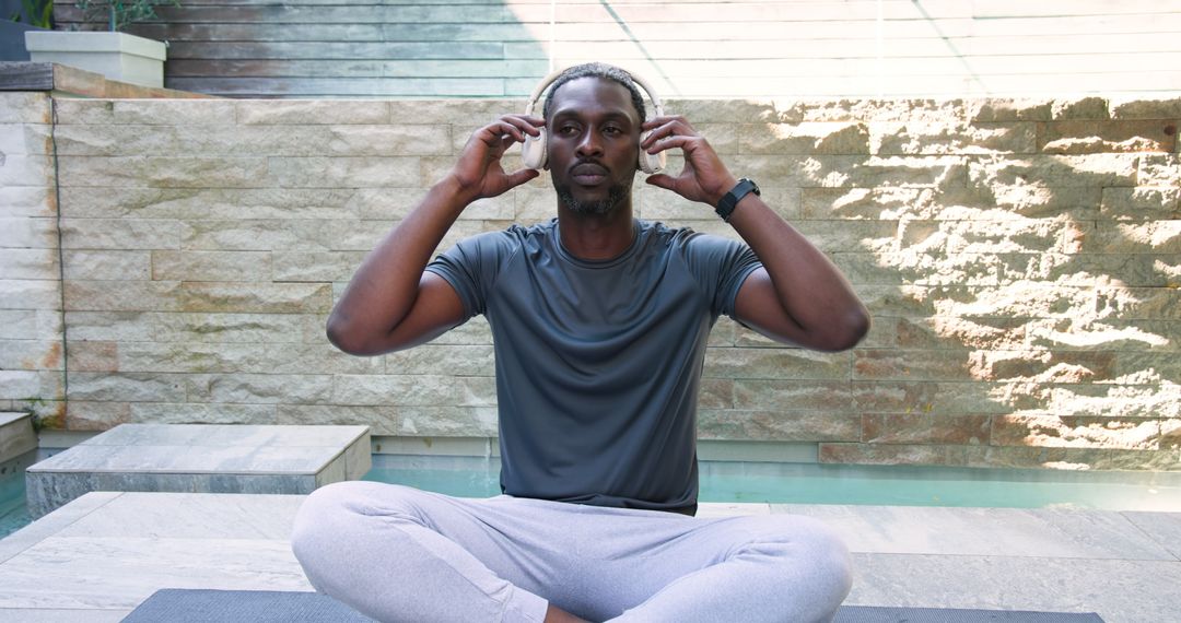 Man Engaging in Meditation and Wellness With Headphones by Poolside