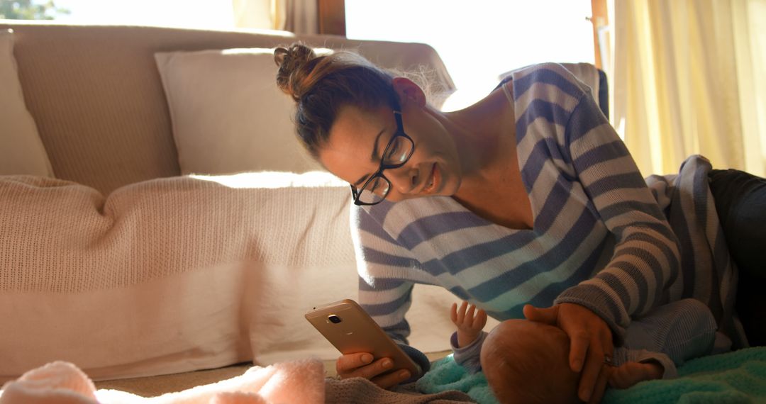 Laughing Mother Laying on Floor Using Smartphone Beside Newborn Baby in Cozy Living Room - Free Images, Stock Photos and Pictures on Pikwizard.com