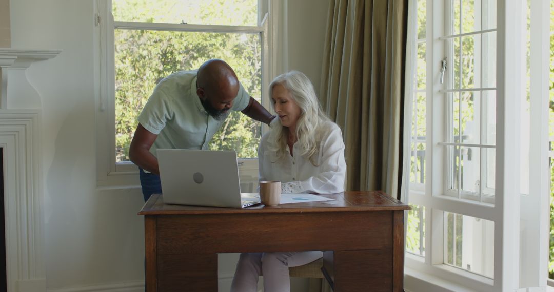 Mature Man Assisting Senior Woman with Laptop at Home