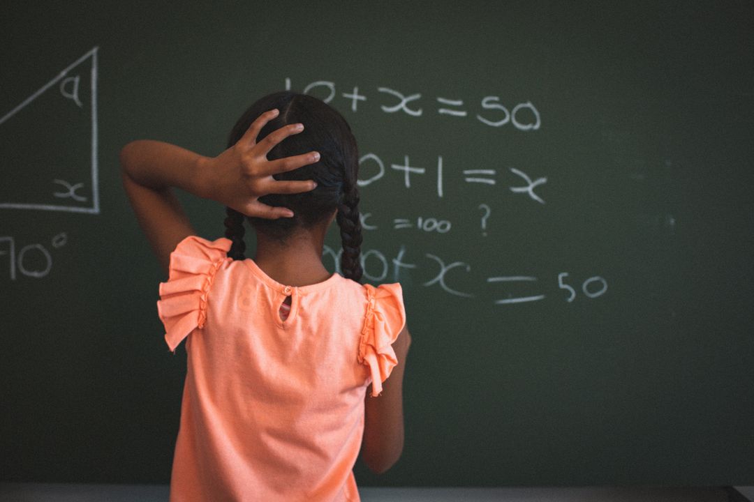 Rear view of biracial schoolgirl standing at maths chalkboard in classroom holding head - Free Images, Stock Photos and Pictures on Pikwizard.com