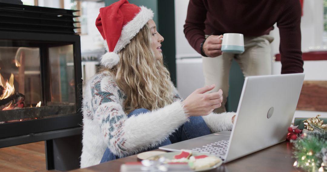 Woman in festive sweater using laptop near fireplace at Christmas - Free Images, Stock Photos and Pictures on Pikwizard.com