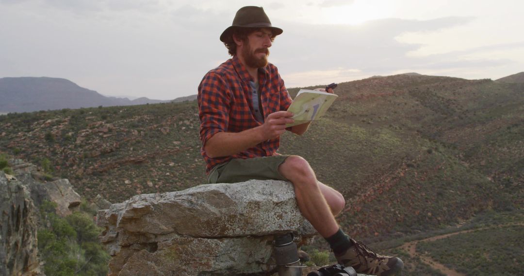 Bearded hiker studying map on canyon rim at sunset, rugged wilderness adventure