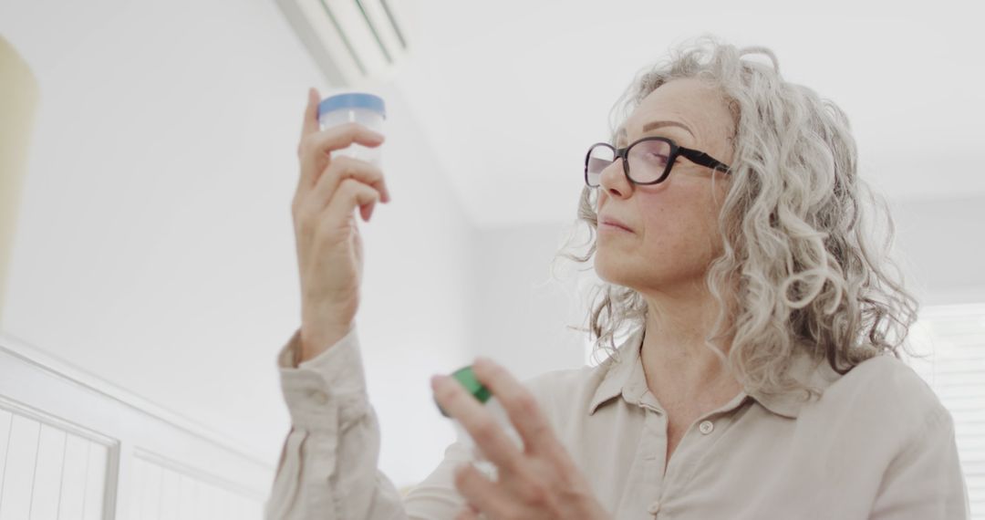 Senior Woman with Gray Hair Examining Skincare Product Indoors - Free Images, Stock Photos and Pictures on Pikwizard.com