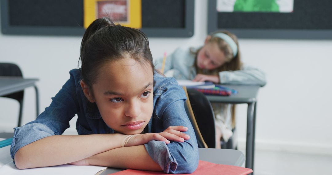 Bored Schoolgirl Leaning on Desk in Classroom