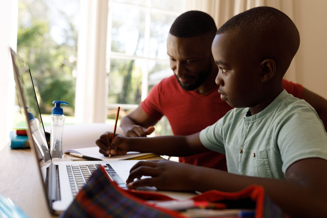 Side view of an african-american boy studying on a laptop with his father beside him helping - Free Images, Stock Photos and Pictures on Pikwizard.com