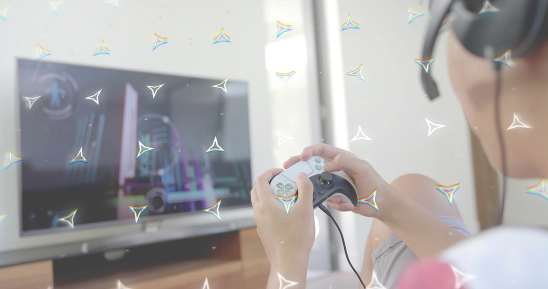 Asian man playing video games holding wired controller wearing headset on sofa with TV