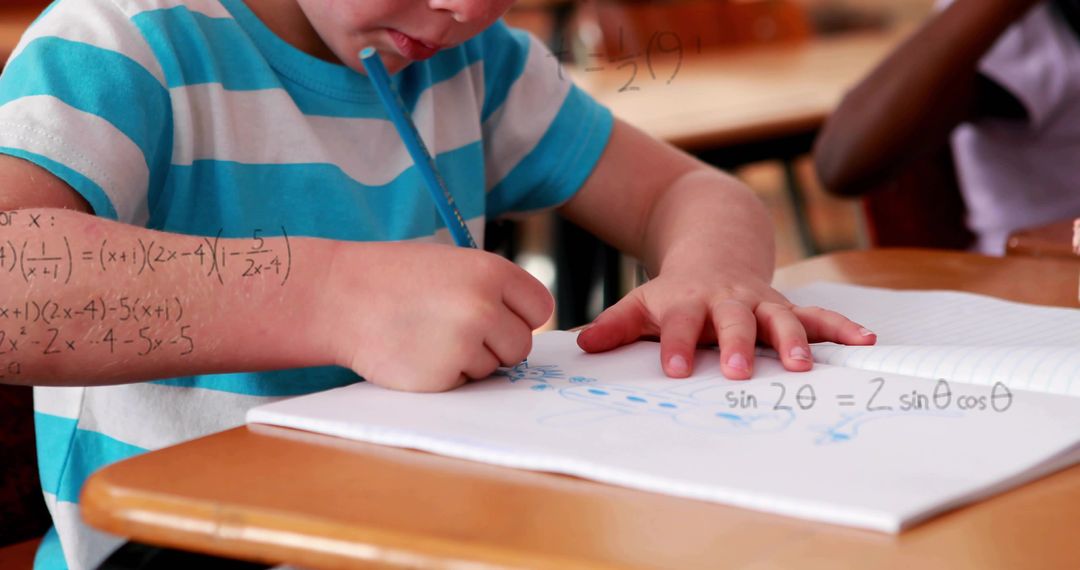 Elementary student writing math equations in spiral notebook at classroom desk, learning