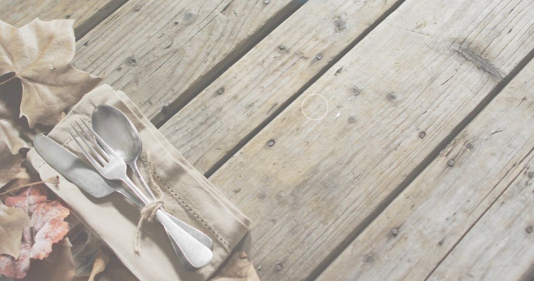 Tied silverware resting on weathered wooden deck with autumn leaves and beige napkin