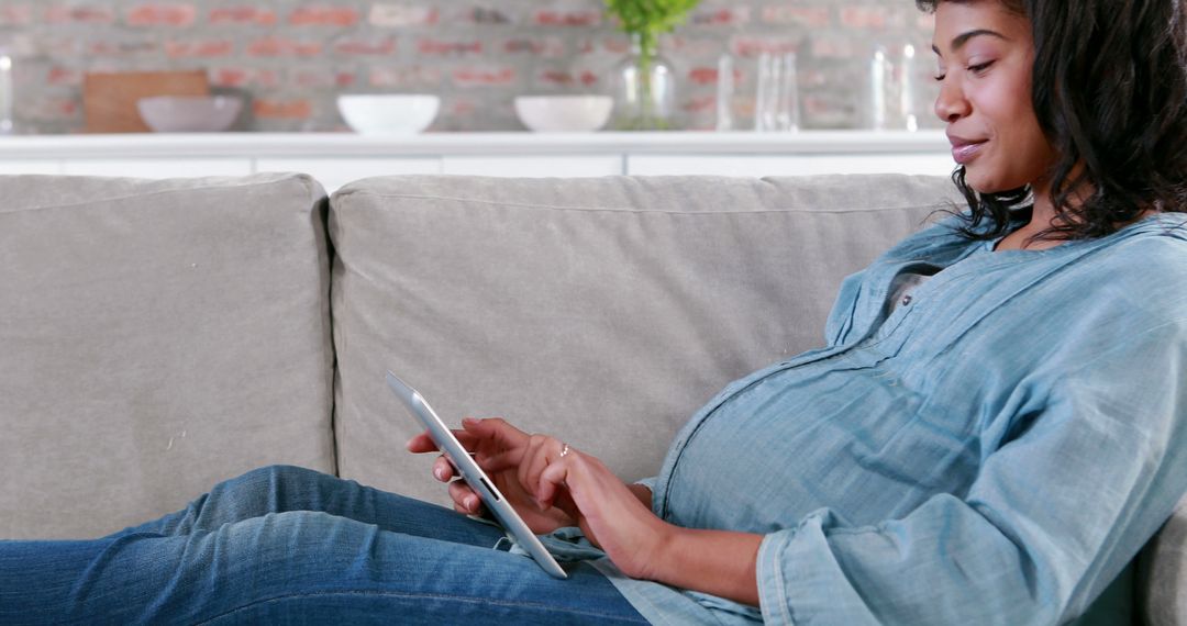 Pregnant Woman Relaxing on Sofa Using Digital Tablet in Modern Home Setting - Free Images, Stock Photos and Pictures on Pikwizard.com