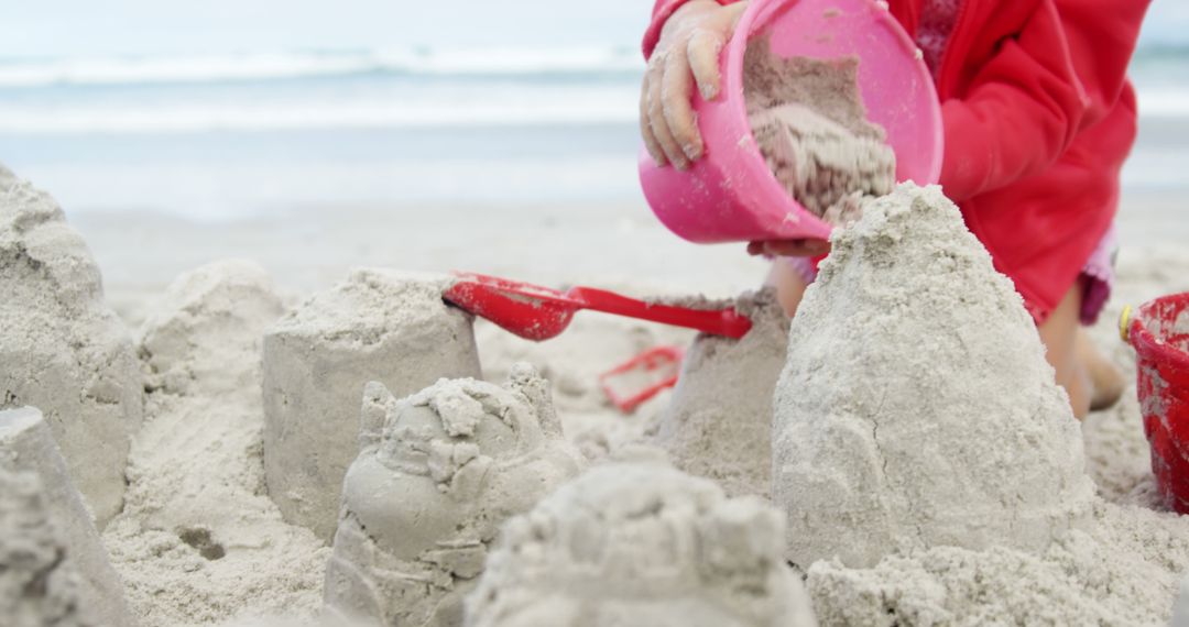 Child Building Sandcastle at Beach with Red Bucket - Free Images, Stock Photos and Pictures on Pikwizard.com