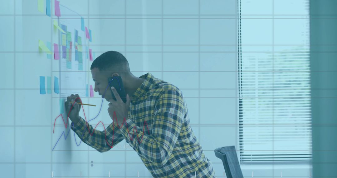 Man in Plaid Shirt Innovating with Graph on Glass Wall in Modern Office