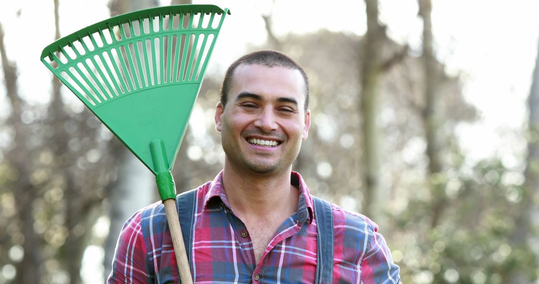 Smiling Young Man Holding Green Rake in Backyard - Free Images, Stock Photos and Pictures on Pikwizard.com