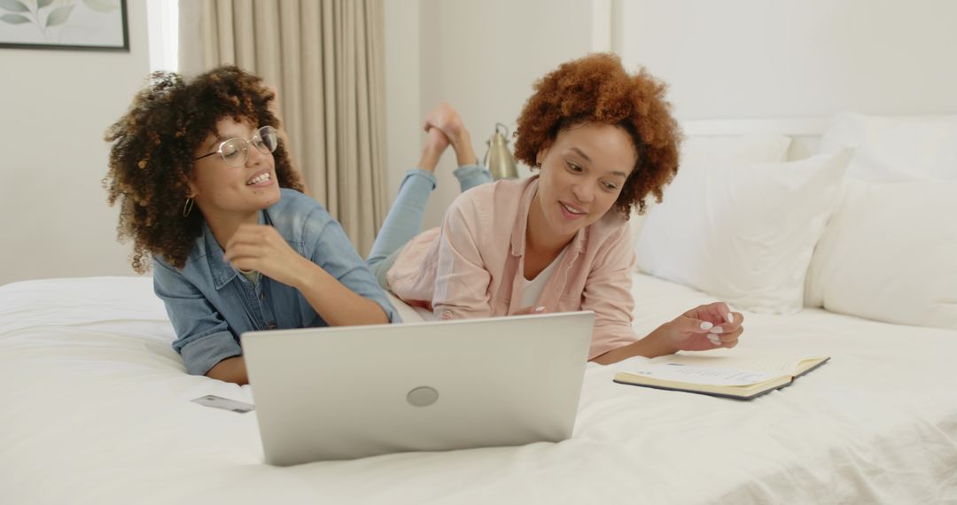 Two Women Lying on Bed Using Laptop and Taking Notes for Remote Work and Study