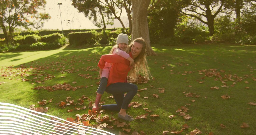 Mother giving daughter piggyback in autumn park with sunlight and fallen leaves