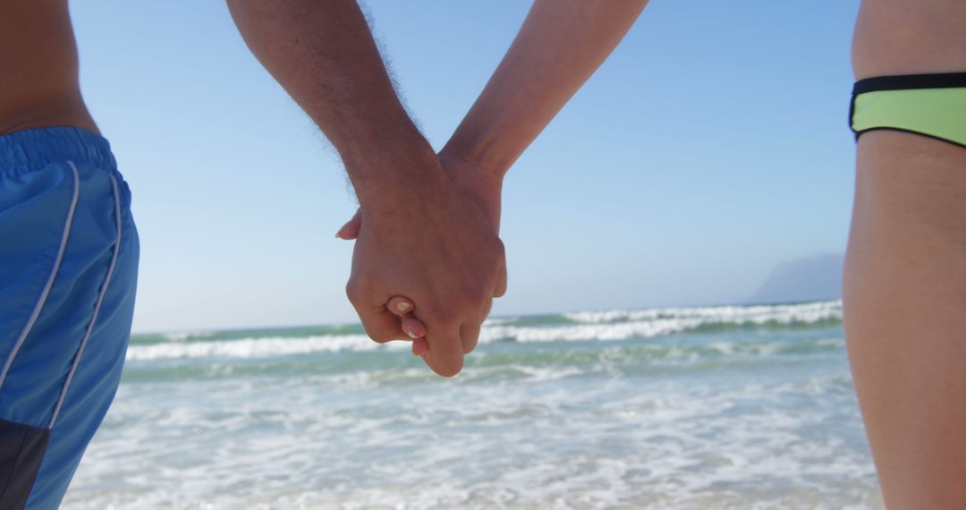 A Caucasian couple holds hands on a sunny beach, with copy space - Free Images, Stock Photos and Pictures on Pikwizard.com