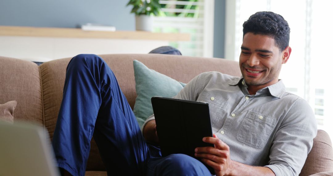 Relaxed Man Smiling and Using Tablet on Sofa at Home - Free Images, Stock Photos and Pictures on Pikwizard.com