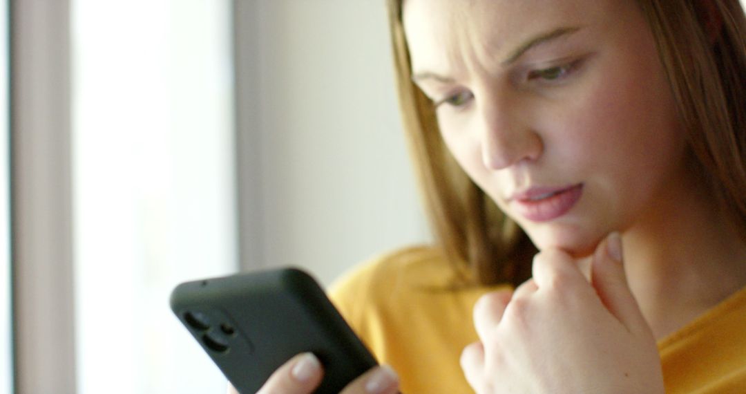 Young Woman Concentrating on Smartphone Screen Indoors - Free Images, Stock Photos and Pictures on Pikwizard.com