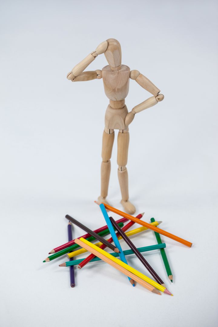 Confused wooden figurine standing near a heap of color pencils - Free Images, Stock Photos and Pictures on Pikwizard.com