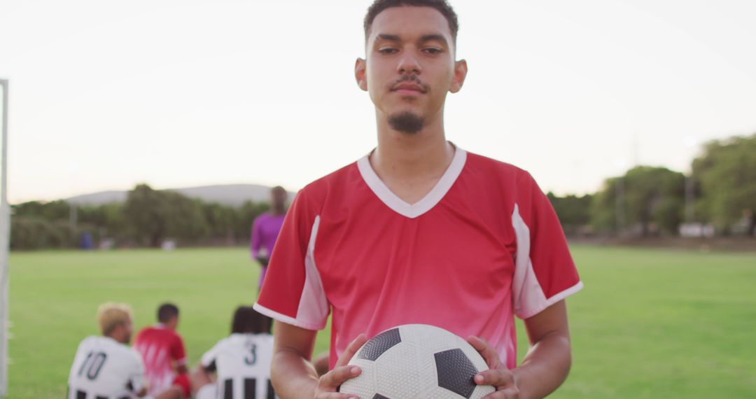 Young Soccer Player Holding Ball on Field with Teammates in Background - Free Images, Stock Photos and Pictures on Pikwizard.com