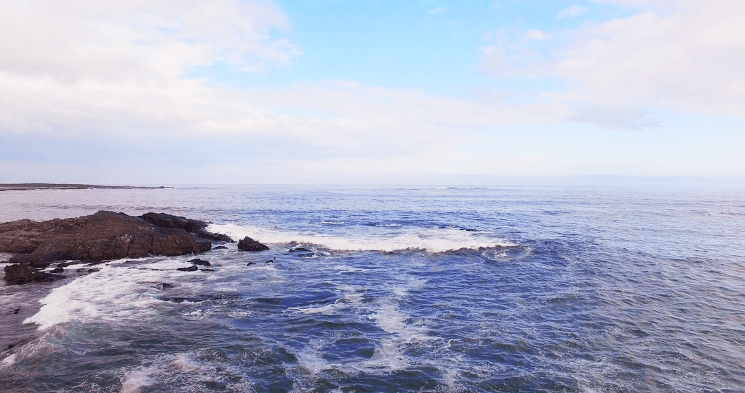 Transparent Waves Crashing on Rocky Shoreline with Blue Sky